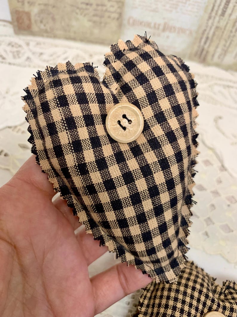 May include: A black and tan gingham heart-shaped pillow with a wooden button. The pillow has a frayed edge.