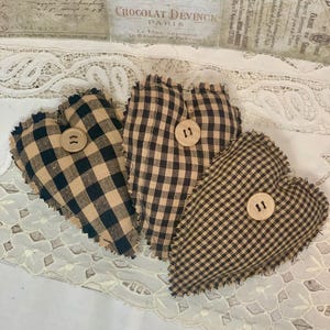 May include: Three brown and black gingham heart-shaped pillows with frayed edges and wooden buttons.