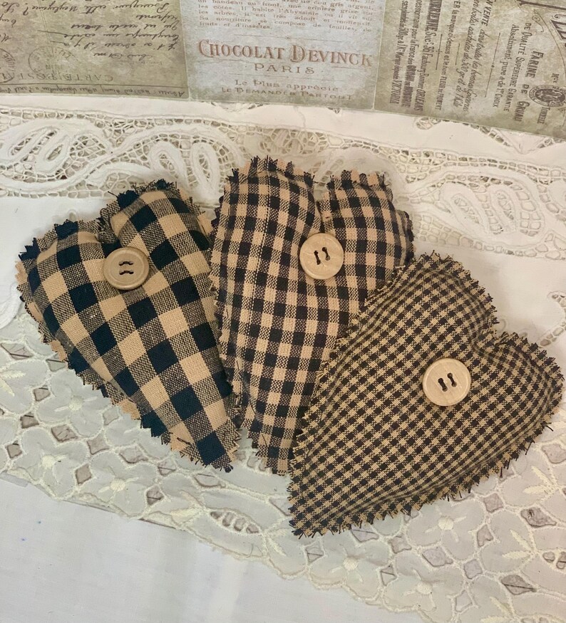 May include: Three brown and black gingham heart-shaped pillows with frayed edges and wooden buttons.