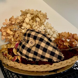 May include: A black and tan checkered heart-shaped pillow with a wooden button in the center, sitting in a woven basket filled with dried flowers.