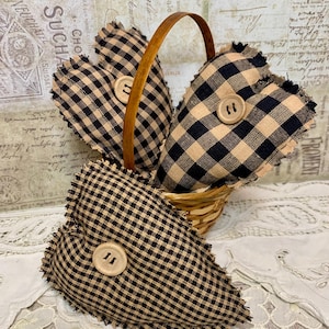 May include: Three black and tan gingham heart-shaped pillows with frayed edges and wooden buttons in a woven basket.