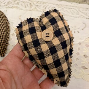 May include: A black and tan gingham heart-shaped pillow with a wooden button. The pillow has a frayed edge.