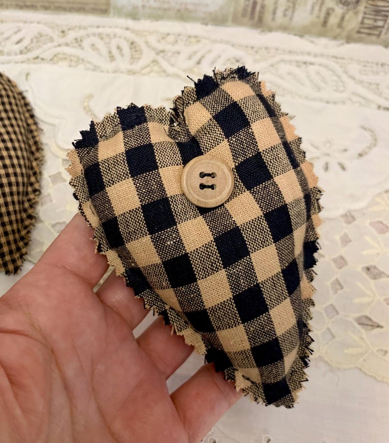 May include: A black and tan gingham heart-shaped pillow with a wooden button. The pillow has a frayed edge.