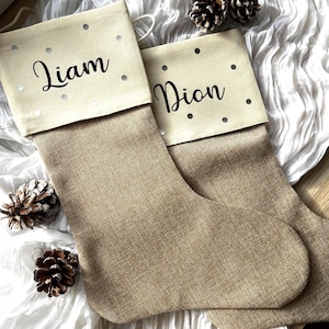 May include: Two beige Christmas stockings with white polka dots and the names "Liam" and "Dion" embroidered on the cuff.