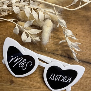 May include: White heart-shaped sunglasses with black lenses. The left lens has the text "M&S" and the right lens has the text "13.07.2024".