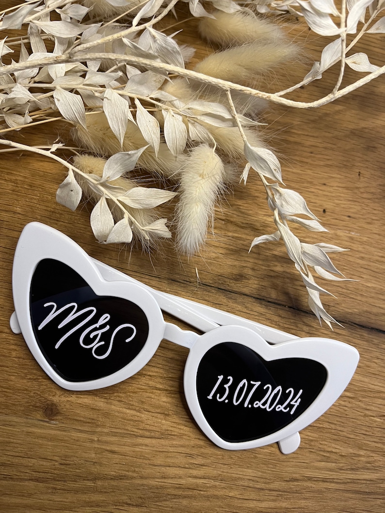 May include: White heart-shaped sunglasses with black lenses. The left lens has the text "M&S" and the right lens has the text "13.07.2024".