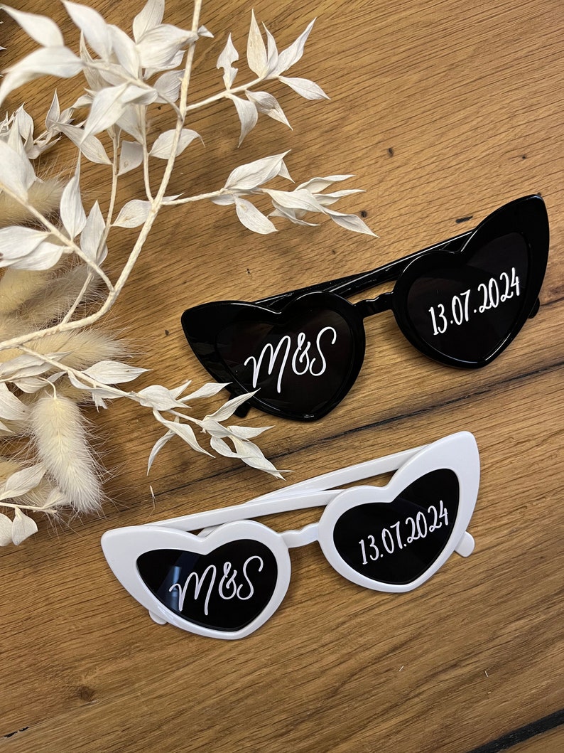 May include: Two pairs of heart-shaped sunglasses, one black and one white, with the initials "M&S" and the date "13.07.2024" printed on the lenses.
