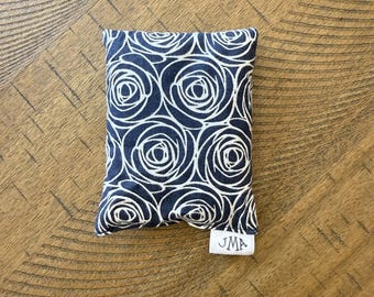 May include: A small, rectangular, blue and white fabric pouch with a white rose pattern. The pouch has a white label with the text "JMA" on it.