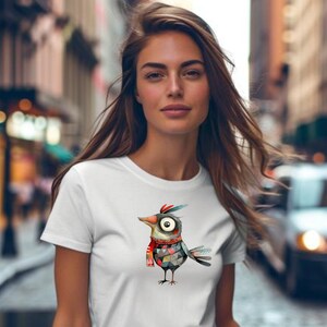 May include: A white t-shirt with a colorful cartoon bird wearing a red scarf. The bird has a large eye and a patterned body.