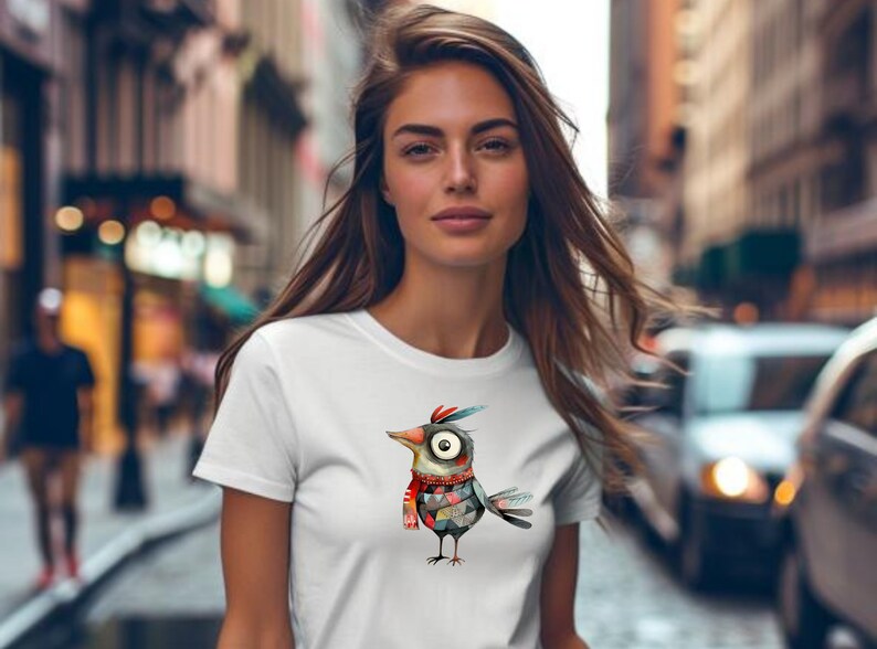 May include: A white t-shirt with a colorful cartoon bird wearing a red scarf. The bird has a large eye and a patterned body.