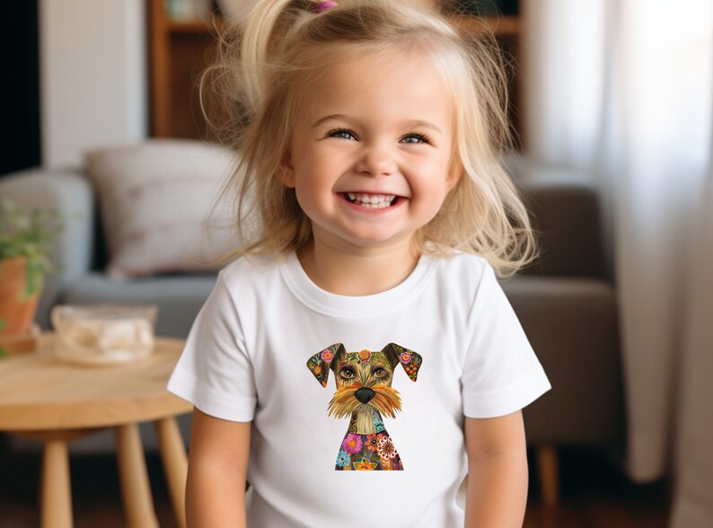 May include: A young child wearing a white t-shirt with a colorful, patterned dog illustration. The dog has a brown and white face with a floral design.