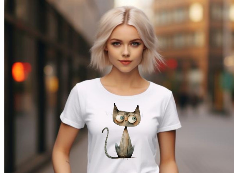 Puede incluir: Camiseta blanca con una ilustraci&oacute;n de dibujos animados de un gato gris con ojos grandes. El gato est&aacute; sentado con la cola enroscada alrededor de sus patas.