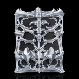 Könnte beinhalten: Eine silberfarbene, rechteckige Box mit einem verzierten, gotisch inspirierten Design. Die Box weist ein zentrales, wirbelsäulenartiges Element und symmetrische, wirbelnde Muster auf. Der Hintergrund ist schwarz und hebt die metallische Oberfläche und die komplizierten Details hervor.