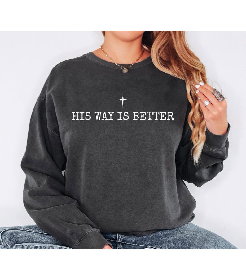 May include: Dark gray sweatshirt with the text "HIS WAY IS BETTER" in white, along with a white cross symbol above the text. The sweatshirt has long sleeves and a crew neck.