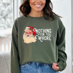 May include: Olive green sweatshirt featuring a vintage Santa Claus graphic with the text "NOTHING FOR YOU WHORE" in white. The Santa illustration includes a red hat, white beard, and rosy cheeks. The sweatshirt is a casual, long-sleeved garment.