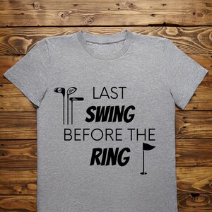 May include: Gray t-shirt with black text that reads "Last Swing Before The Ring" with a golf club and flag graphic.