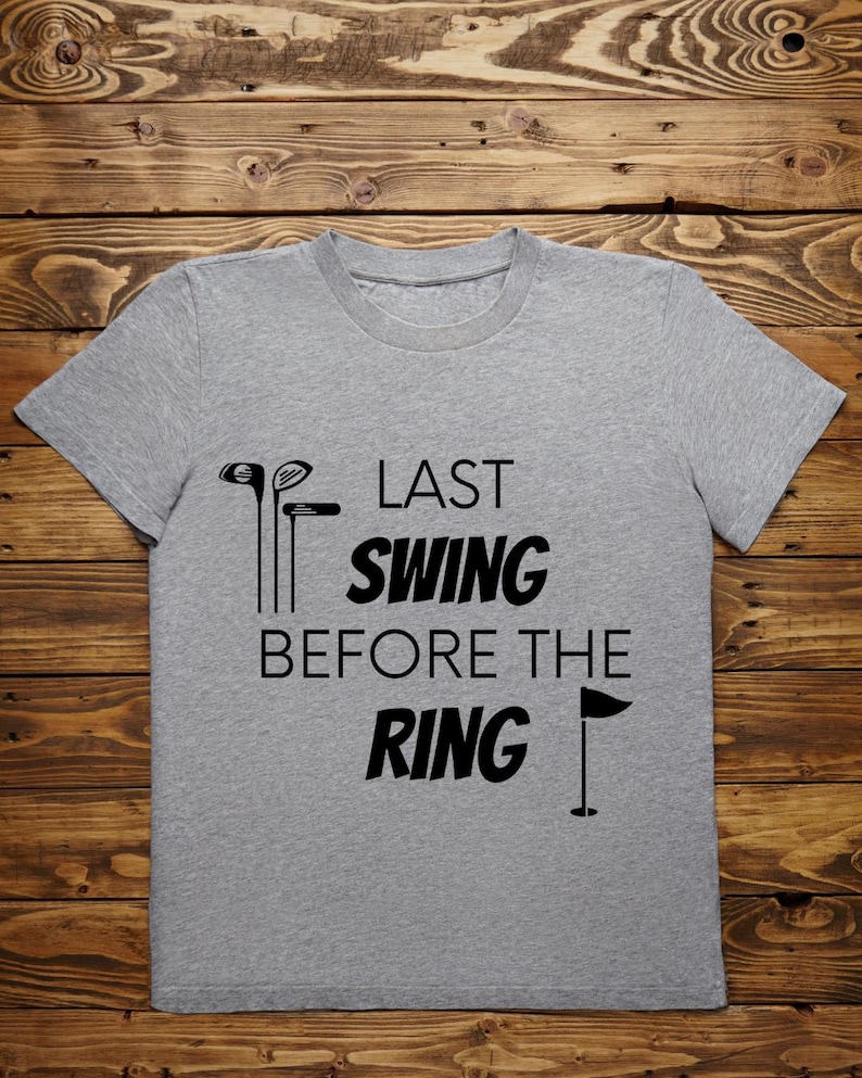 May include: Gray t-shirt with black text that reads "Last Swing Before The Ring" with a golf club and flag graphic.