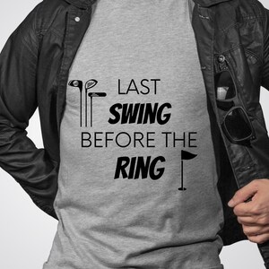 May include: A gray t-shirt with the text "Last Swing Before The Ring" and a golf club and flag graphic.