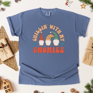 Puede incluir: Una camiseta azul con el texto "Chillin' with my Gnomies" en naranja, beige y verde. El gr&aacute;fico presenta tres gnomos con sombreros coloridos. La camiseta est&aacute; rodeada de decoraciones navide&ntilde;as.
