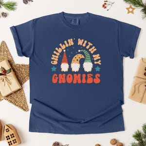Puede incluir: Camiseta azul marino con el texto "Chillin' with my Gnomies" y un gr&aacute;fico de tres gnomos. Los gnomos tienen barbas blancas y llevan sombreros. La camiseta est&aacute; rodeada de decoraciones navide&ntilde;as.