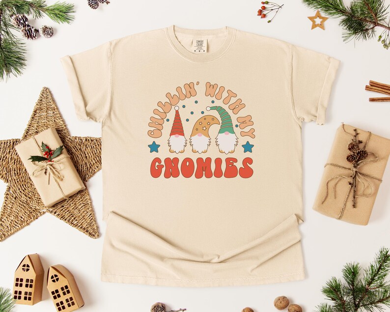 Puede incluir: Camiseta color crema con el texto "Chillin' with my Gnomies" en una fuente retro. El gr&aacute;fico presenta tres gnomos con sombreros rojos, beige y verdes. La camiseta es de estilo casual y unisex.