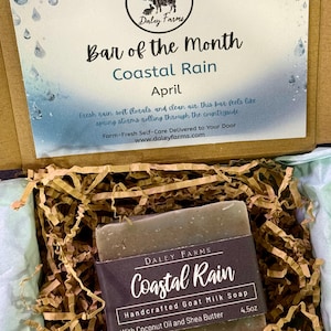 May include: A bar of Coastal Rain goat milk soap, 4.5 oz, in a box with paper filler. The box includes a card with the Daley Farms logo and text: "Bar of the Month, Coastal Rain, April". The soap is handcrafted with coconut oil and shea butter.