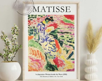 May include: A framed print of Matisse's "La Japonaise: Woman beside the Water (1905)". The artwork features a colorful, abstract depiction of a woman near water, with vibrant hues of red, green, blue, and yellow. The print is displayed in a white frame.