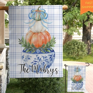 May include: A blue and white checkered garden flag with a stack of pumpkins in a blue and white porcelain bowl. The pumpkins are decorated with green leaves and a blue ribbon. The text "The Mabrys" is printed on the flag.