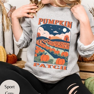 May include: Sport grey sweatshirt with a "Pumpkin Patch" graphic. The design features a field of orange pumpkins under a blue sky with a full moon. The text "Pumpkin Patch" is in an orange, vintage-style font.