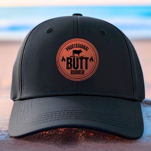 May include: Black baseball cap with a brown leather patch that says "Professional Butt Rubber" with a pig silhouette.