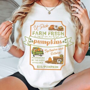May include: White t-shirt with a graphic of a vintage truck carrying pumpkins and the text "U Pick Farm Fresh Pumpkins", "September and October", and "$15/Pumpkin".