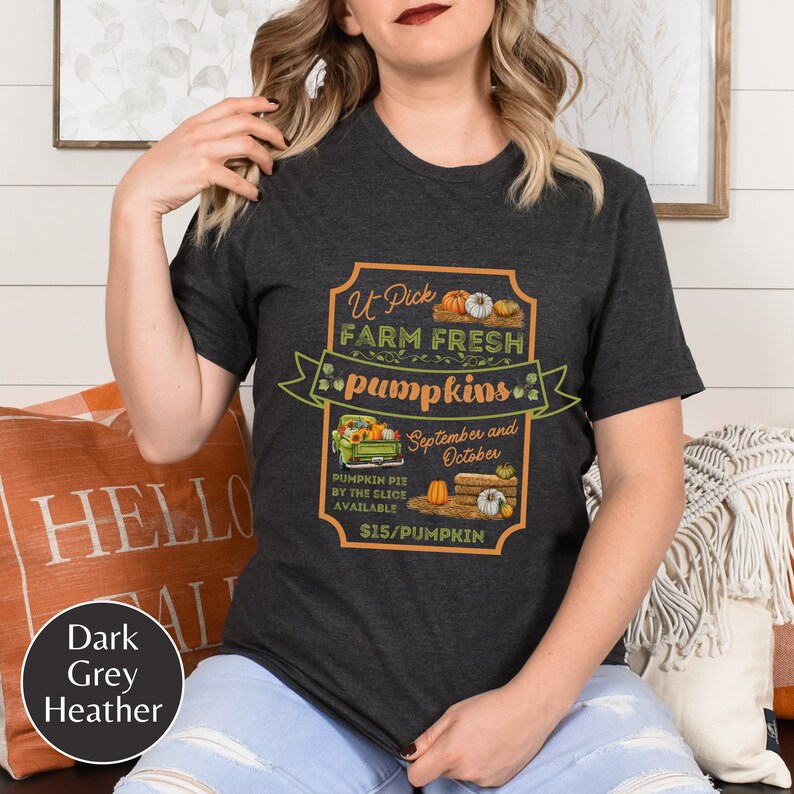 May include: A dark grey heather t-shirt with a vintage-style graphic of a pickup truck carrying pumpkins. The graphic says "U-Pick Farm Fresh Pumpkins" and "September and October". It also says "Pumpkin Pie by the Slice Available $15/Pumpkin".