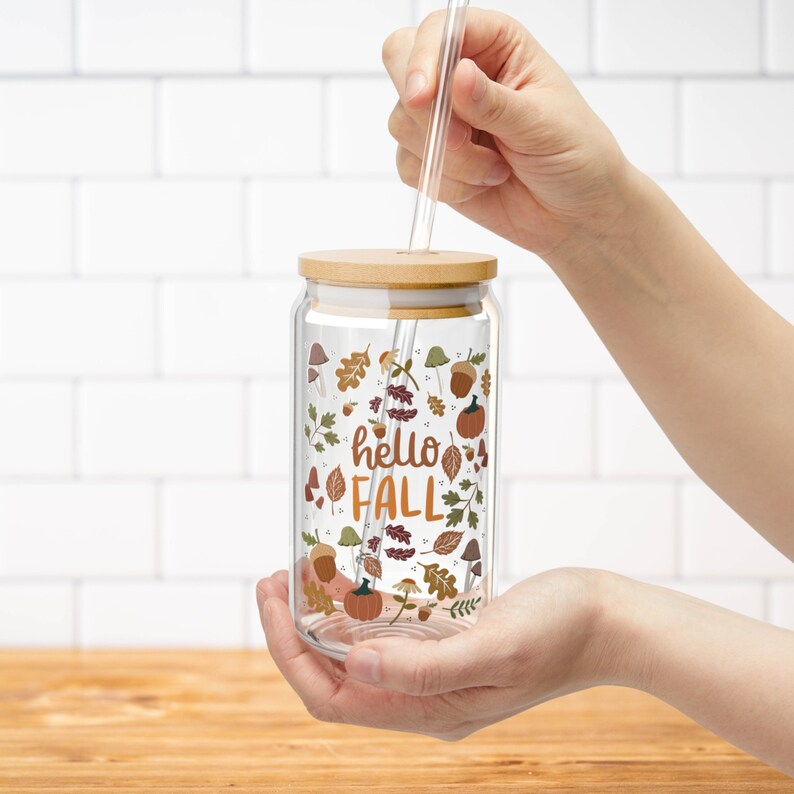 May include: A clear glass water bottle with a bamboo lid and a straw. The bottle has a fall-themed design with leaves, acorns, and the text "hello fall".
