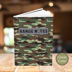 May include: A green, brown, and tan camouflage notebook with the text "RANGE NOTES" on a gray patch. The notebook is on a wooden surface.