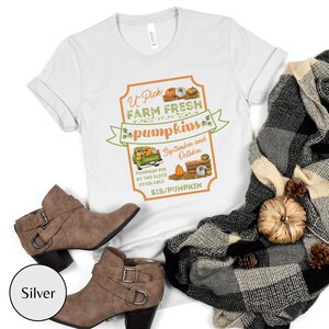 May include: A white t-shirt with a vintage-style sign that says "U-Pick Farm Fresh Pumpkins" with a picture of a truck carrying pumpkins and the text "September and October" and "$15/Pumpkin".
