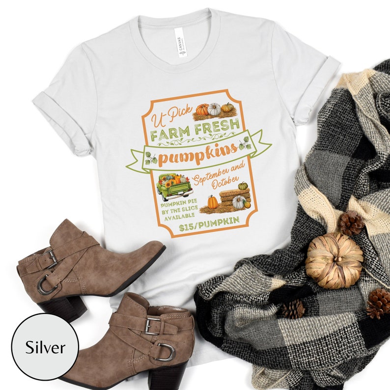 May include: A white t-shirt with a vintage-style sign that says "U-Pick Farm Fresh Pumpkins" with a picture of a truck carrying pumpkins and the text "September and October" and "$15/Pumpkin".