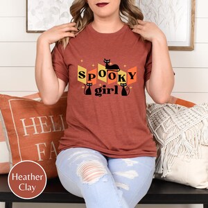 May include: A rust-colored t-shirt with a retro design featuring black cats and the text "Spooky girl".
