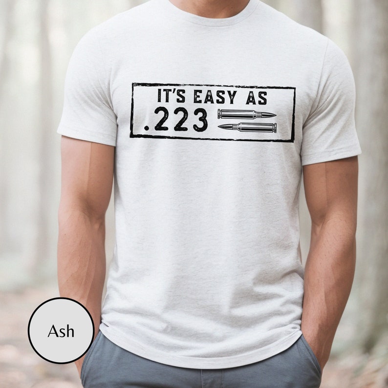 Peut inclure: T-shirt blanc avec un motif noir qui dit "It's easy as .223" avec deux douilles de balle.