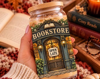 Puede incluir: Un vaso transparente con tapa de bambú y pajita, lleno de una bebida de color marrón claro. El vaso presenta un gráfico colorido de la fachada de una librería con el texto BOOKSTORE y un cartel en la puerta que dice OPEN LATE.