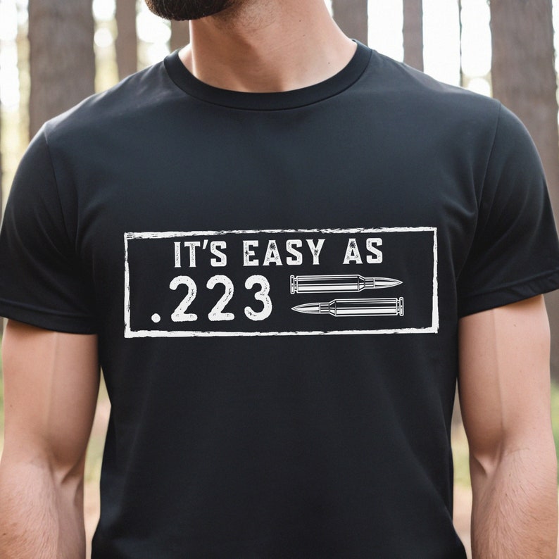 Peut inclure: T-shirt noir avec un rectangle blanc qui dit "It's easy as .223" avec deux douilles de balles &agrave; l'int&eacute;rieur du rectangle.