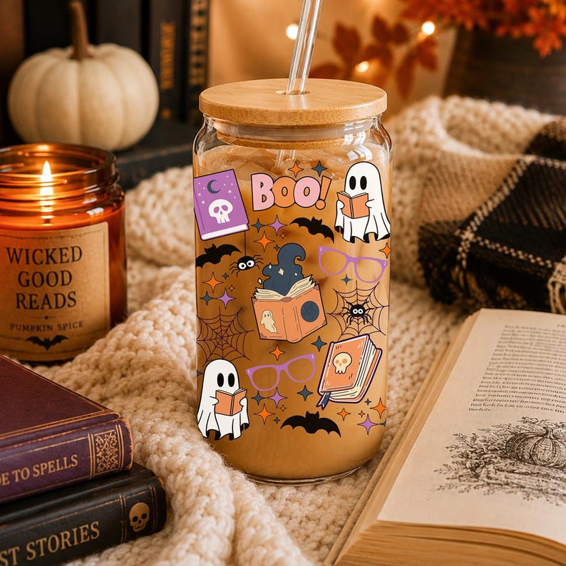 Puede incluir: Un vaso de cristal transparente con tapa de bamb&uacute; y pajita de cristal, lleno de caf&eacute; helado. El exterior presenta gr&aacute;ficos coloridos con tem&aacute;tica de Halloween que incluyen fantasmas, libros, ara&ntilde;as, murci&eacute;lagos, gafas moradas y el texto BOO en letras rosas.