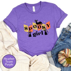 May include: Purple t-shirt with a black cat and the text "Spooky girl" in a retro style.