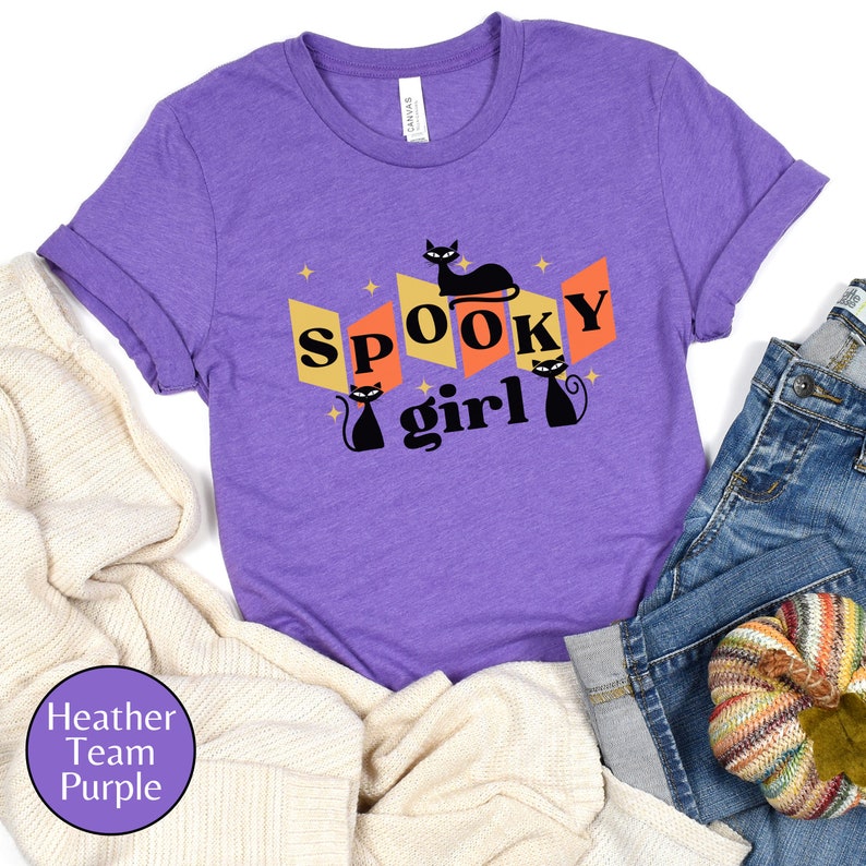 May include: Purple t-shirt with a black cat and the text "Spooky girl" in a retro style.