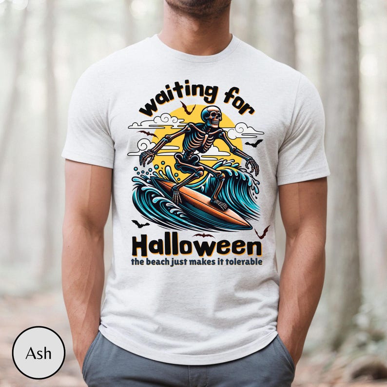 May include: Ash-colored t-shirt featuring a surfing skeleton graphic. The design includes the words "waiting for Halloween" above the skeleton and "the beach just makes it tolerable" below. The skeleton is riding a surfboard on a wave.