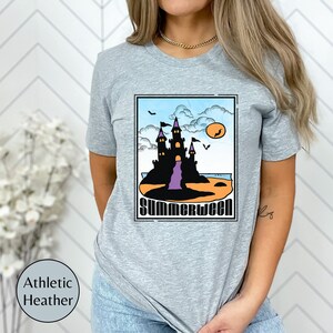 Pu&ograve; includere: Una t-shirt color grigio melange con una grafica di un castello nero su una spiaggia con il testo "Summerween" in un font retr&ograve;.