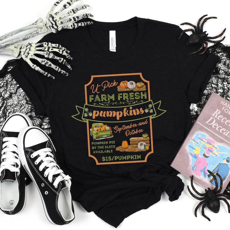 May include: Black t-shirt with a graphic of a sign that says "U Pick Farm Fresh Pumpkins" with a picture of a truck with pumpkins and the text "September and October" and "$15/PUMPKIN".