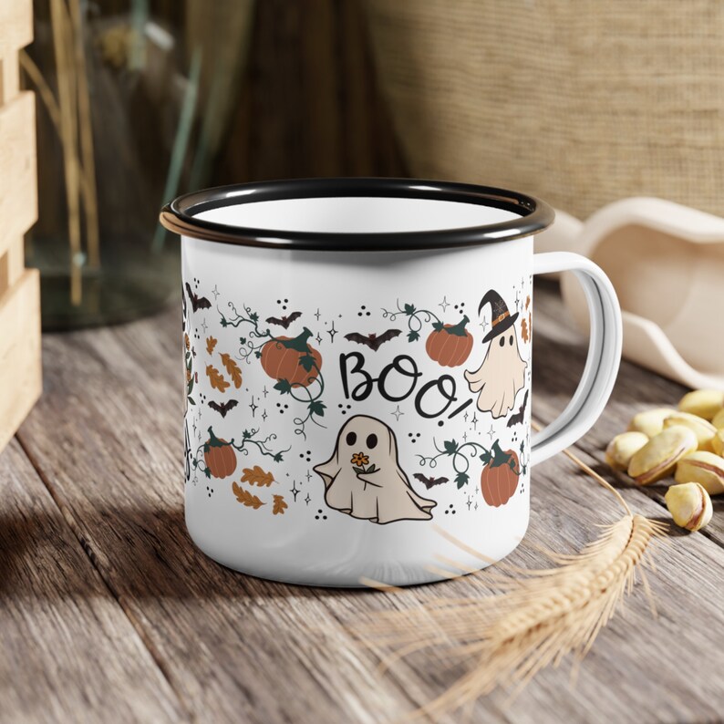 May include: White enamel mug with a black rim and handle. The mug features a Halloween-themed design with ghosts, pumpkins, and the word "BOO!" in black lettering.