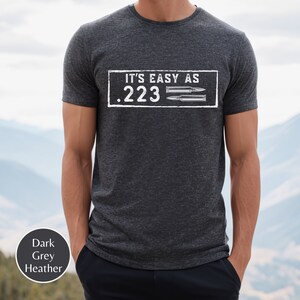 Peut inclure: Un t-shirt en gris chin&eacute; fonc&eacute; avec le texte "IT'S EASY AS .223" et deux douilles de balles imprim&eacute;es sur le devant.