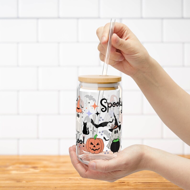 May include: A clear glass jar with a wooden lid and a straw. The jar has a Halloween-themed design with ghosts, bats, pumpkins, and the words "Spooky Boo!" printed on it.
