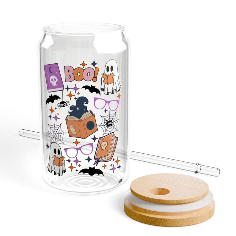 Puede incluir: Un vaso transparente con forma de lata, tapa de bamb&uacute; y pajita de cristal, con un estampado colorido de tem&aacute;tica Halloween que incluye fantasmas, libros, ara&ntilde;as, murci&eacute;lagos y la palabra BOO! en letras naranjas junto a peque&ntilde;as estrellas.